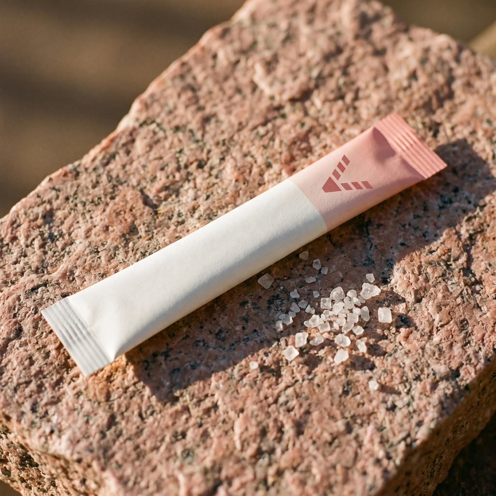 A slim salt-white stick pack with a pale grapefruit-pink end, printed with the VitaminHill mark, on pink granite, coarse salt crystals beside it.
