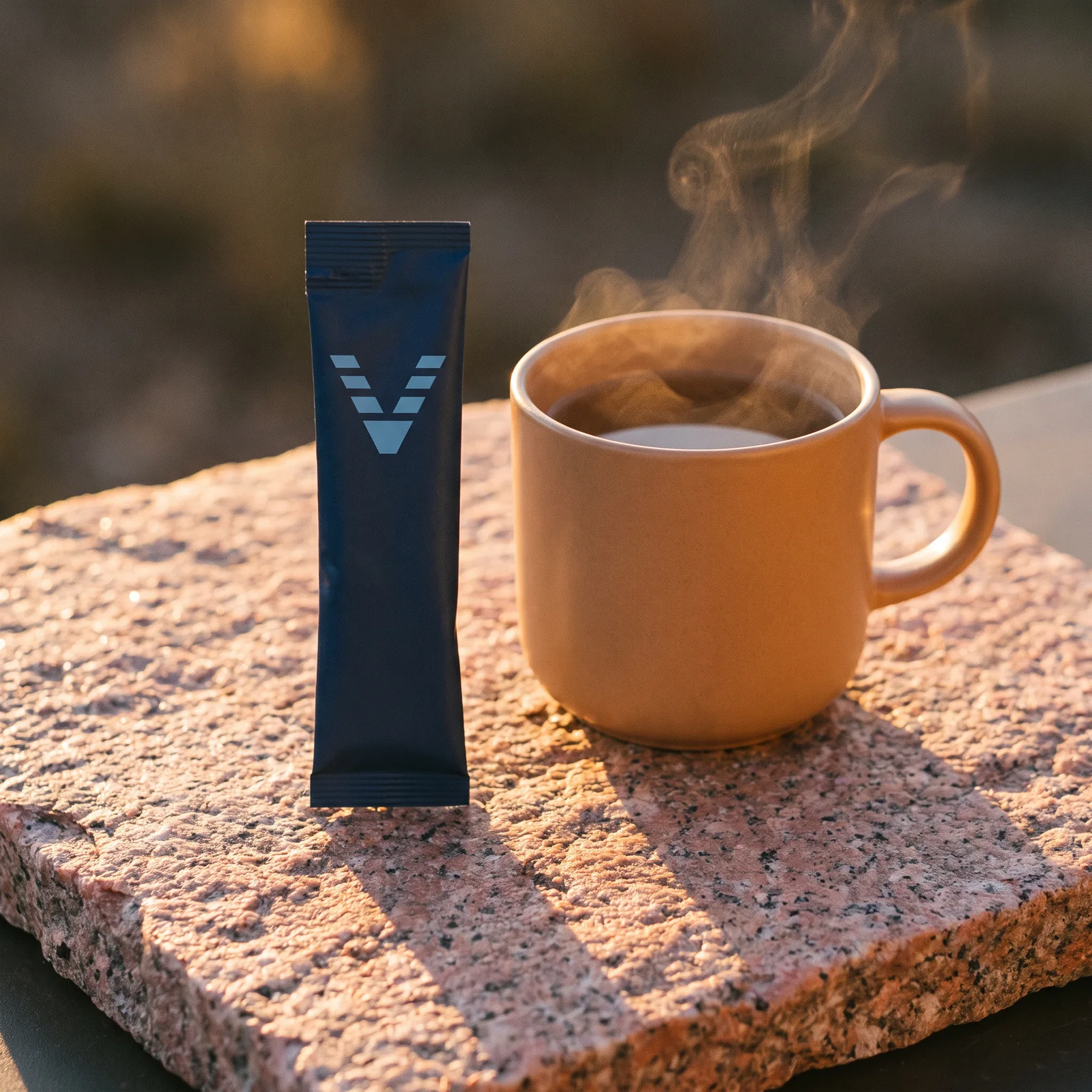 A solid midnight blue stick pack with the VitaminHill mark on pink granite in the last light, a steaming enamel mug beside it.