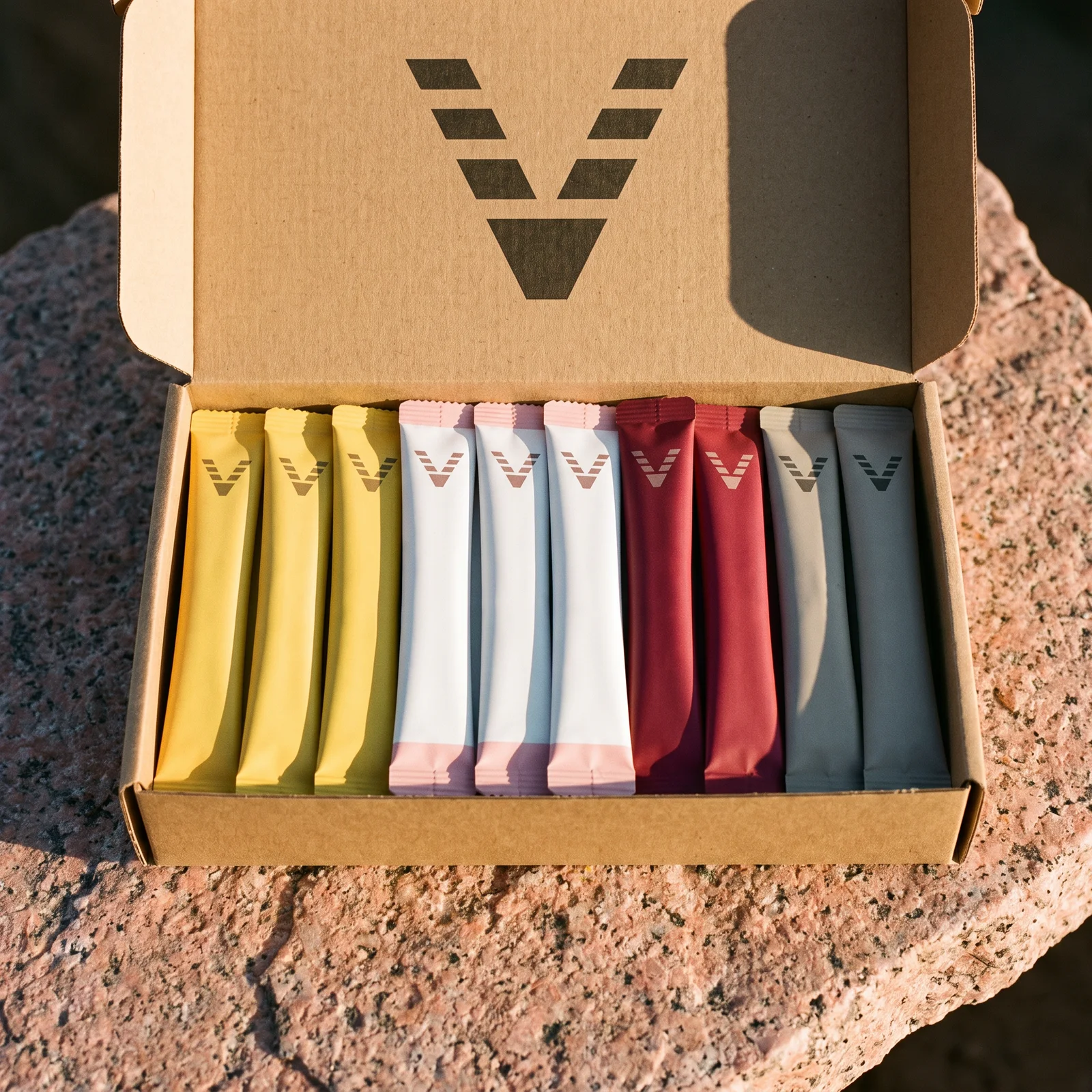 An open kraft carton printed with the VitaminHill mark on pink granite, ten stick packs standing in it: yellow, white with pink ends, red and gray.